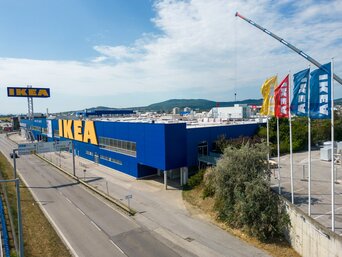 Weitwinkelaufnahme des IKEA Standorts in Vösendorf, der von verschiedenen Flaggen und einer belebten Straße umgeben ist.