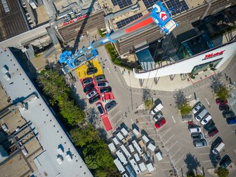 Luftaufnahme eines urbanen Industriegebiets mit mehreren geparkten Autos und einem großflächigen Gebäude, das teilweise mit RLT-Anlagen bedeckt ist. Ein großer Kran erstreckt sich über das Dach.